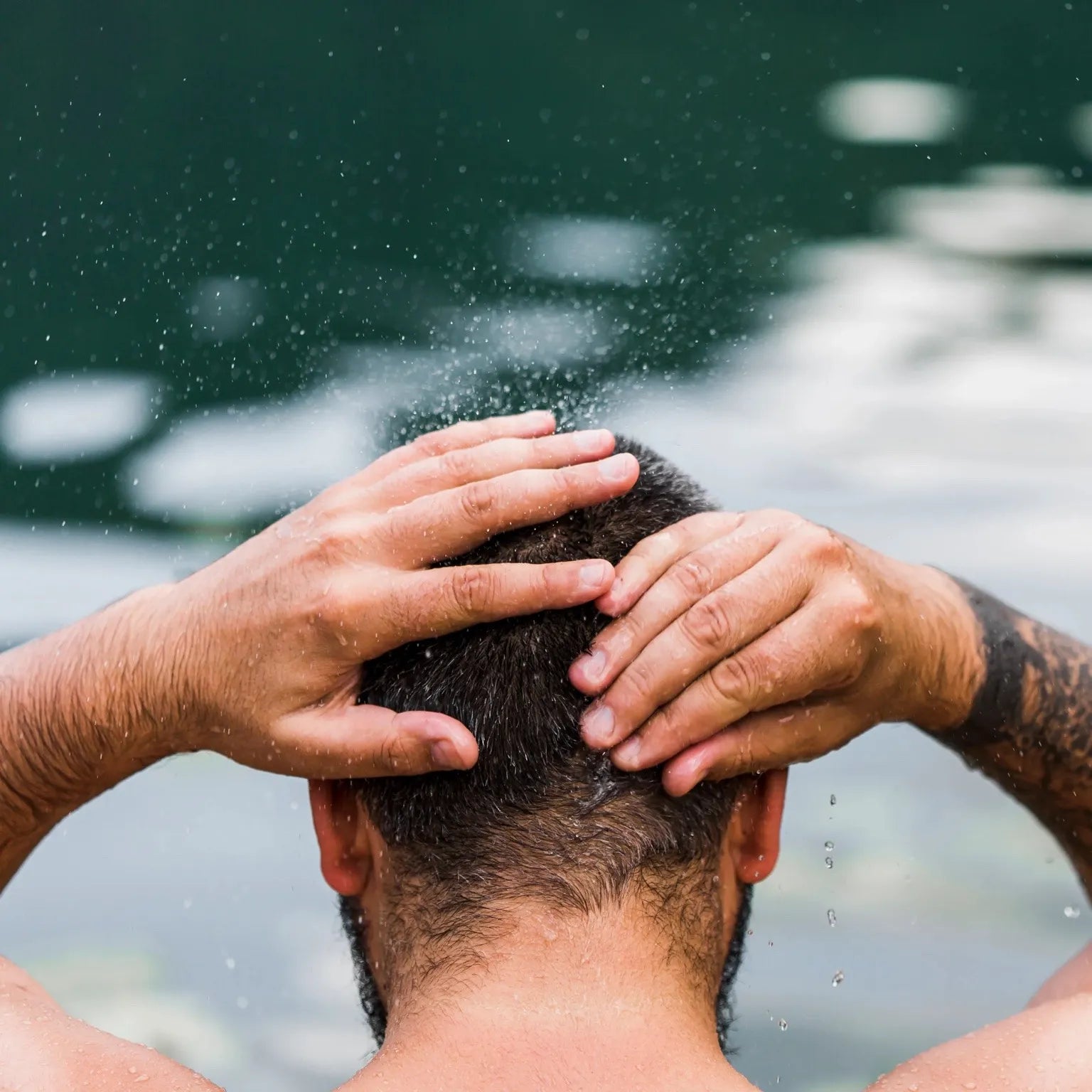 Homme de dos avec les mains dans les cheveux mouillés, illustrant un rituel de coiffure masculine mi-longue après rinçage à l’eau